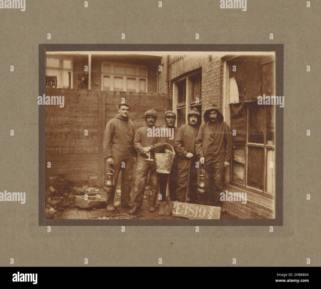 Group portrait of five unknown men in work clothes with gas lamps and a bucket in a backyard, anonymous, Netherlands, c. 1900 - c. 1920, cardboard, gelatin silver print, height 110 mm × width 80 mm Stock Photo