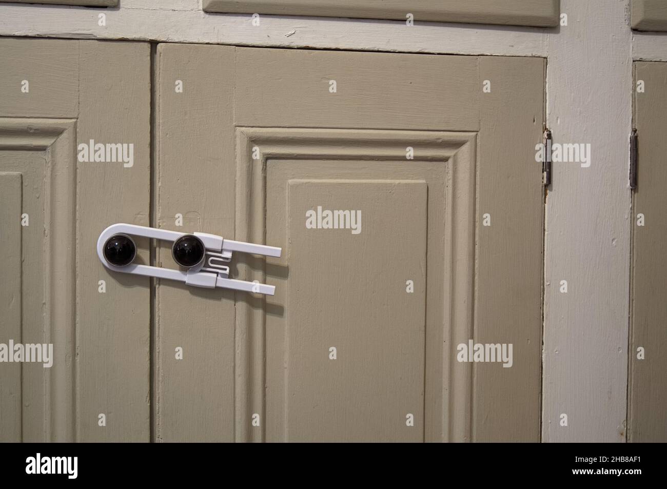A white child safety lock preventing a child from opening the doors of a cabinet, with copy space to the right Stock Photo