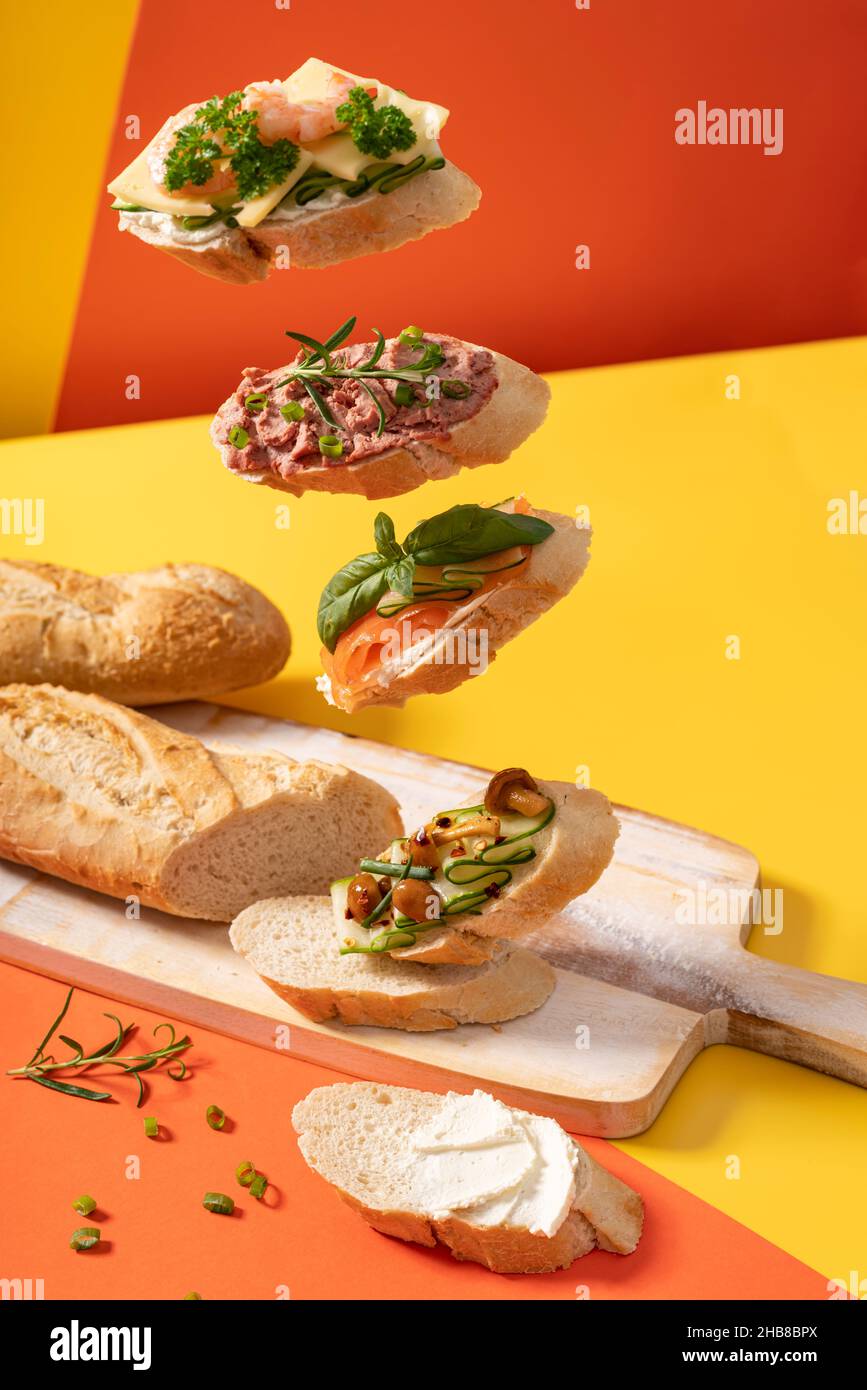Little levitating baguette sandwiches on vibrant yellow and orange background decorated with green leaves Stock Photo