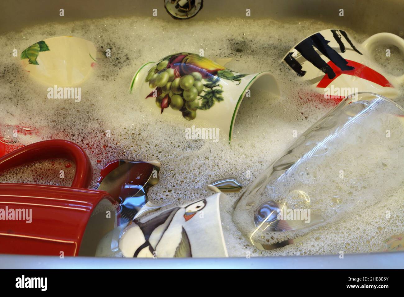 Drinking cups and glass in sink with soap suds Stock Photo
