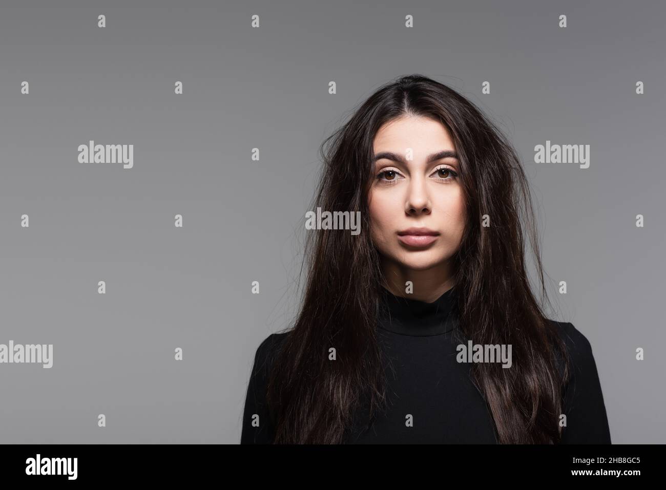 young woman in black turtleneck with tousled hair isolated on grey Stock Photo