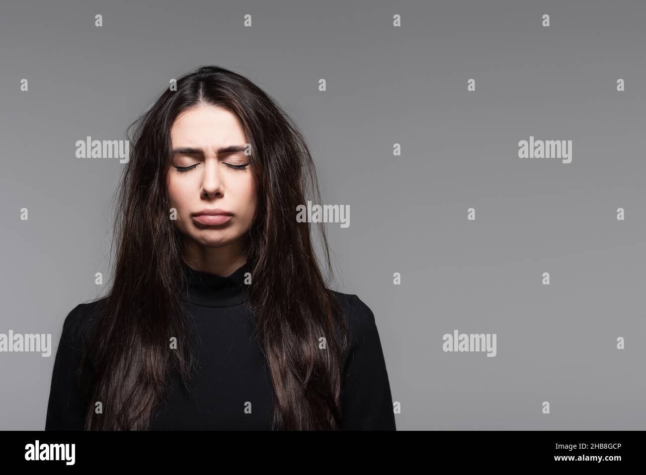 sad young woman in black turtleneck with damaged hair isolated on grey Stock Photo