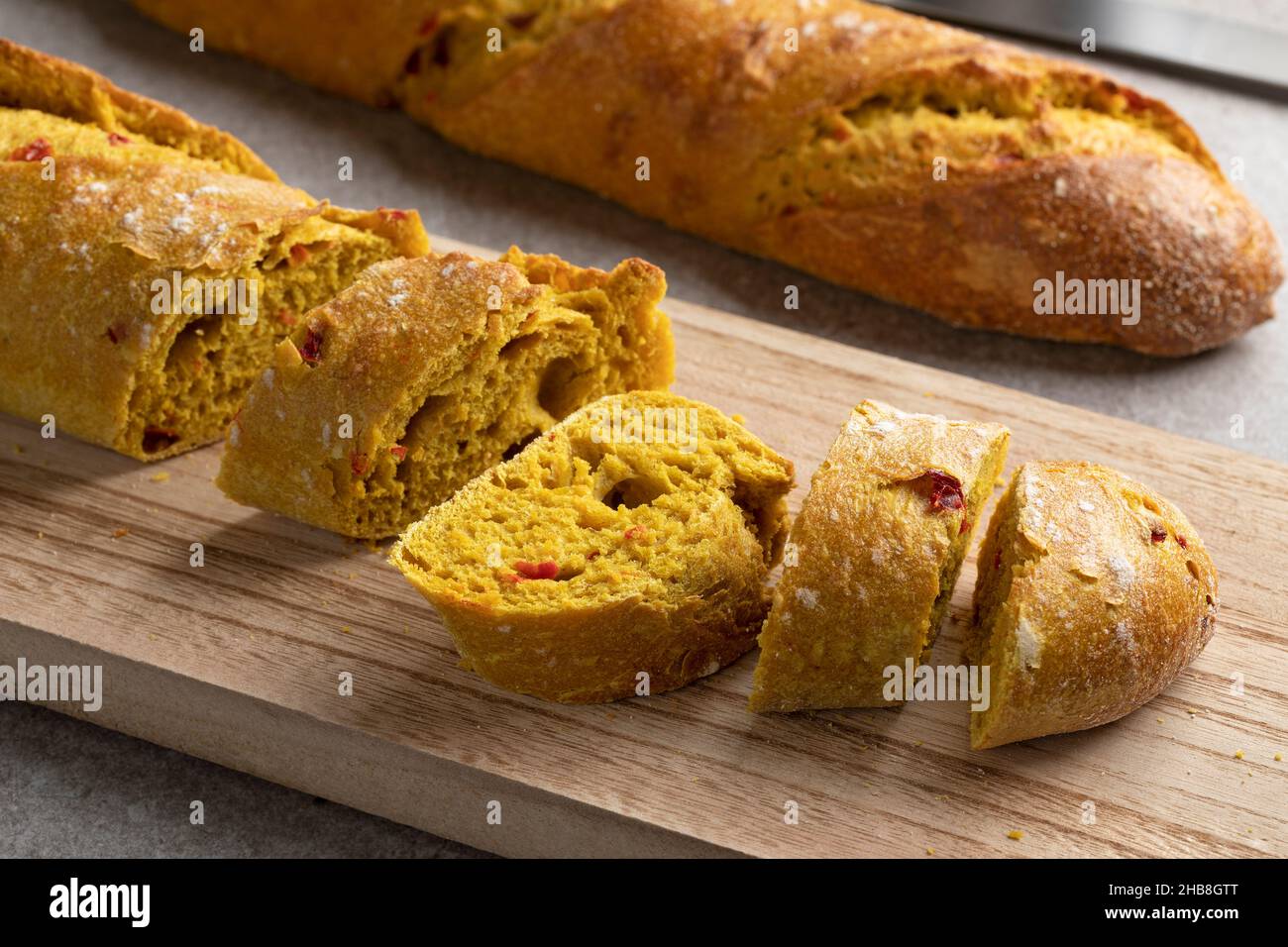 Fresh baked homemade baguette with curry and tomato seasoning close up at a wooden cutting board Stock Photo