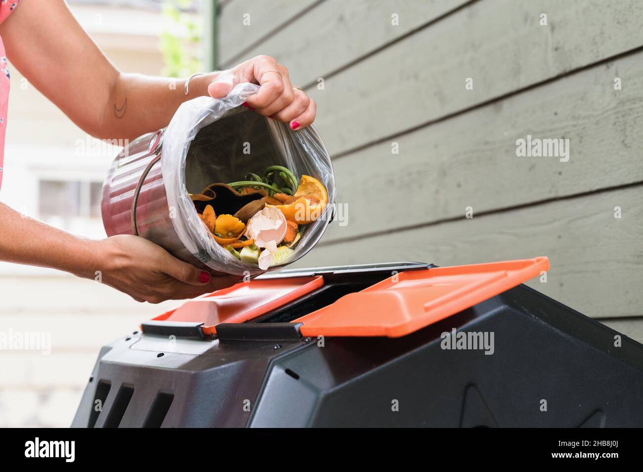 Close-up of woman putting kitchen scraps into compost bin Stock Photo