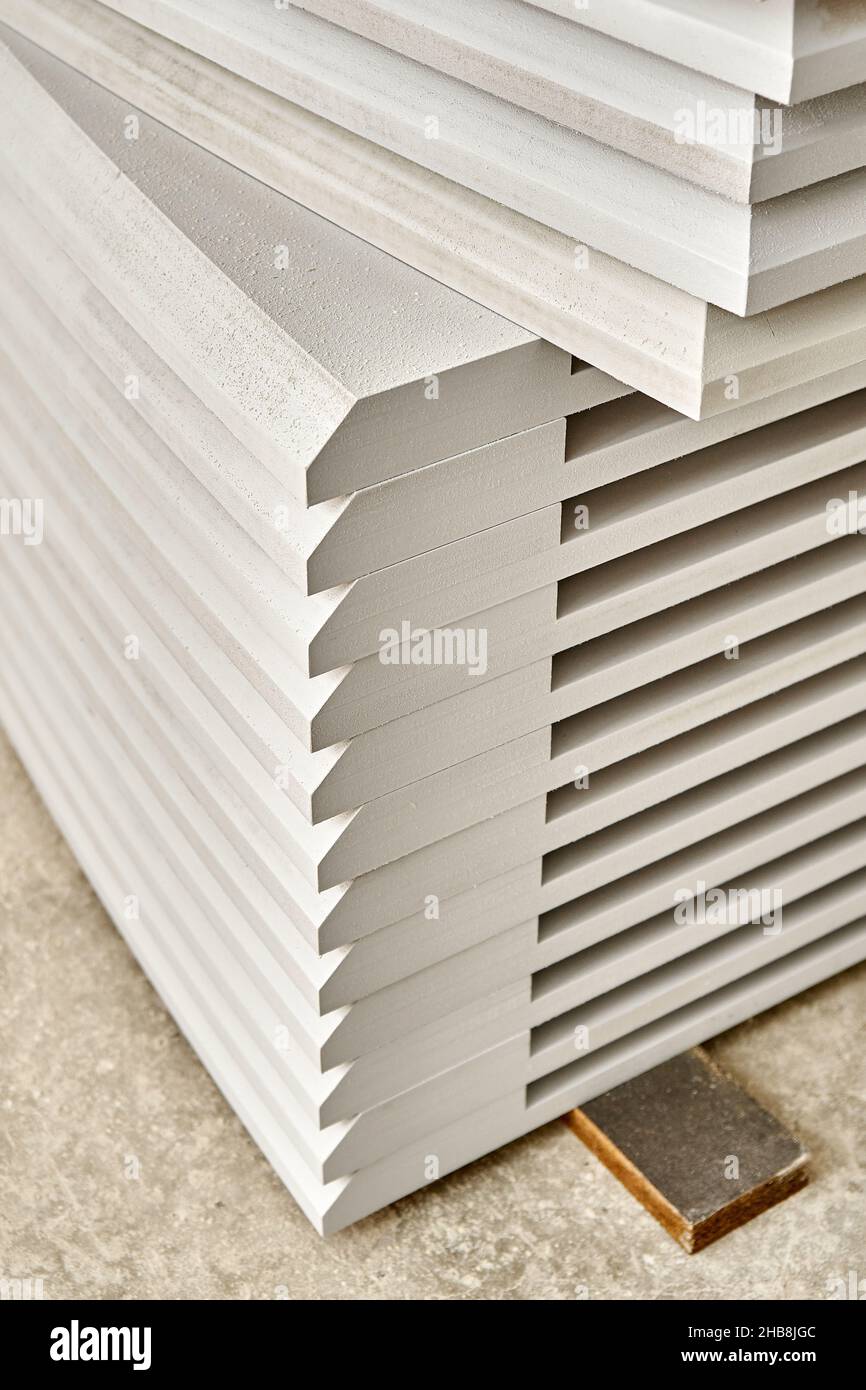 High stack of new tabletops made of mdf covered with white primer stands on floor in sanding workshop extreme closeup Stock Photo