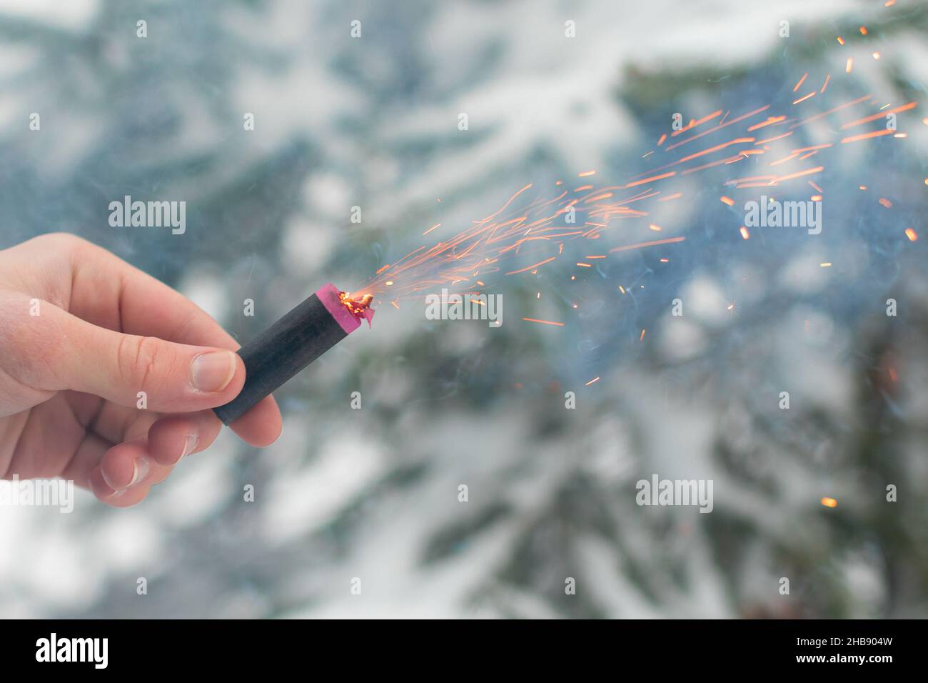 Burning Firecracker in a Hand. Guy Holding a Petard Outdoors in Winter at Daytime. Loud and Dangerous New Year's Entertainment. Hooliganism with Pyrot Stock Photo