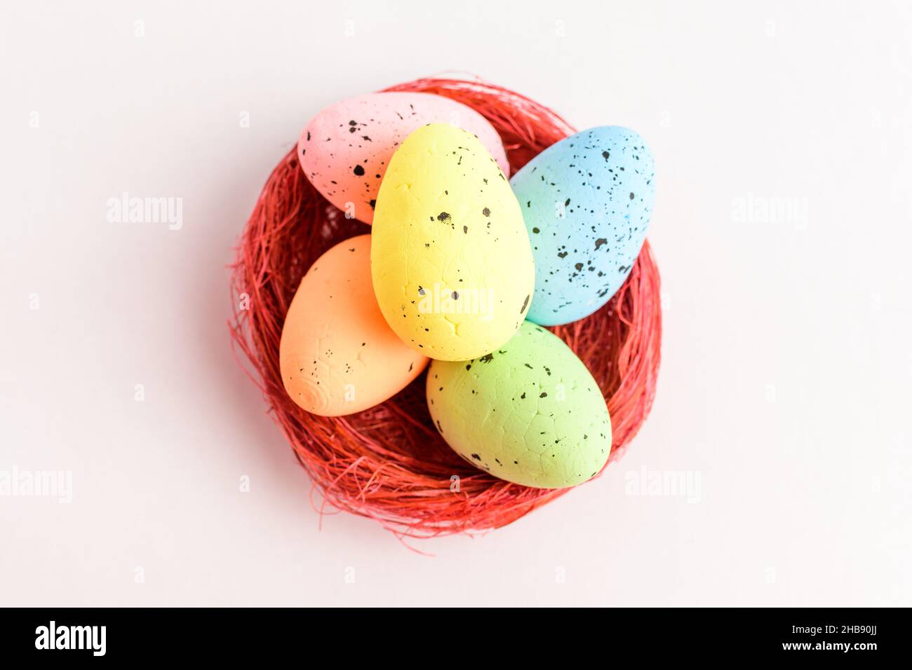 Mixed colored decorative red Easter eggs in a red rustic basket isolated on a white table Stock Photo