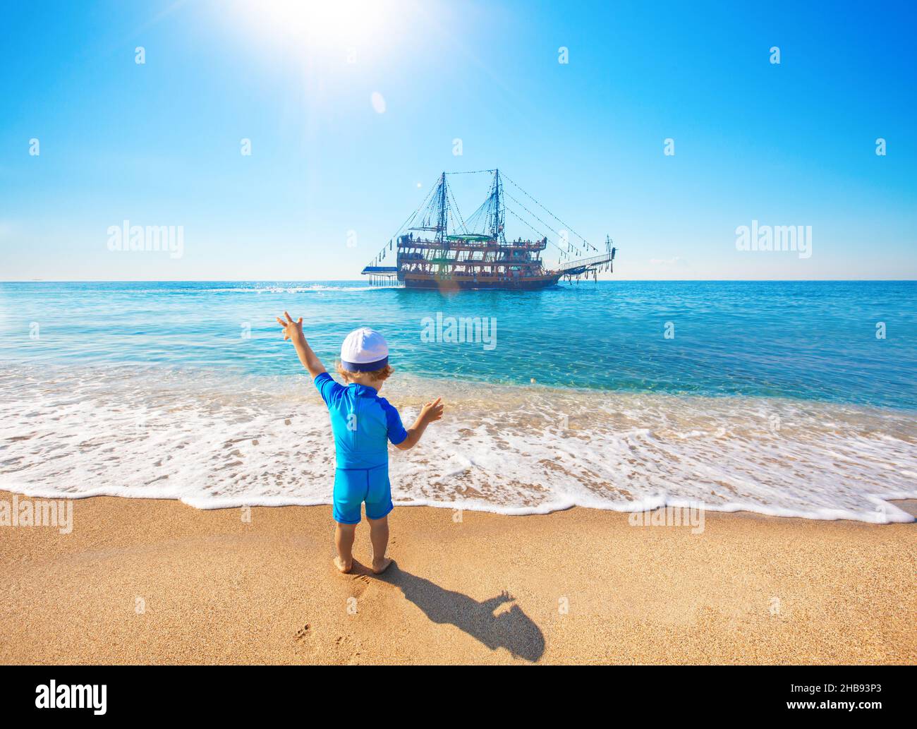 A little child on the beach waves to a sailing ship Stock Photo