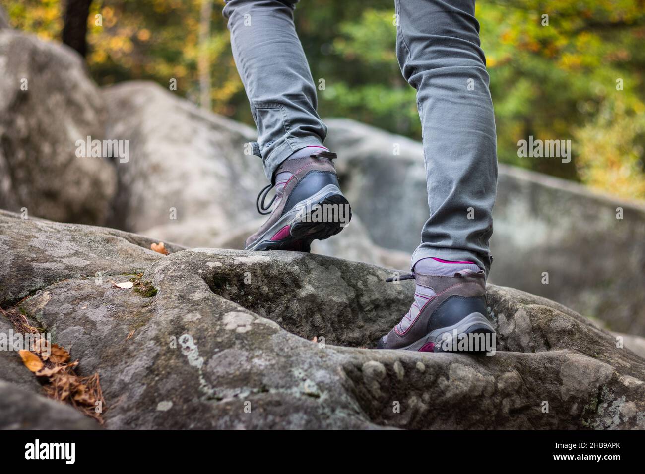 Woman is wearing hiking boot and walking on rocks in forest at autumn. Hiker climbing in mountain Stock Photo