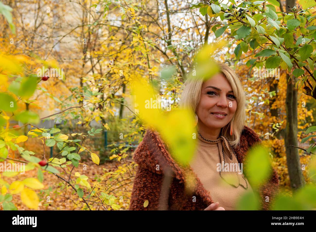 Closeup shot of a beautiful blond female through branches with yellow ...