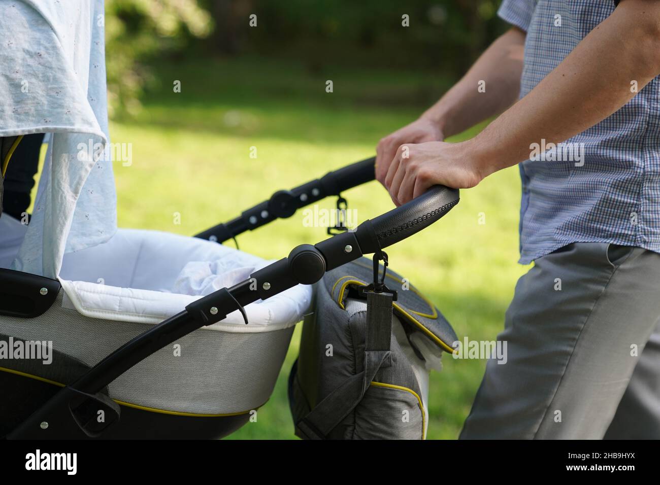Close-up of men's hands with a stroller, a young dad walking in the park with a baby in a stroller, fatherhood, dad, father's day concept. High quality photo Stock Photo