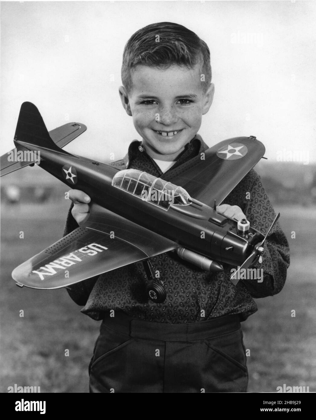 Well dressed young boy posing with his US Army gas engine model airplane while smiling at the camera. Circa 1955 Stock Photo