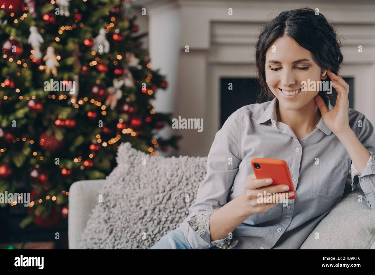 Relaxed happy Italian woman sitting at cozy sofa at home with phone during Christmas holidays Stock Photo