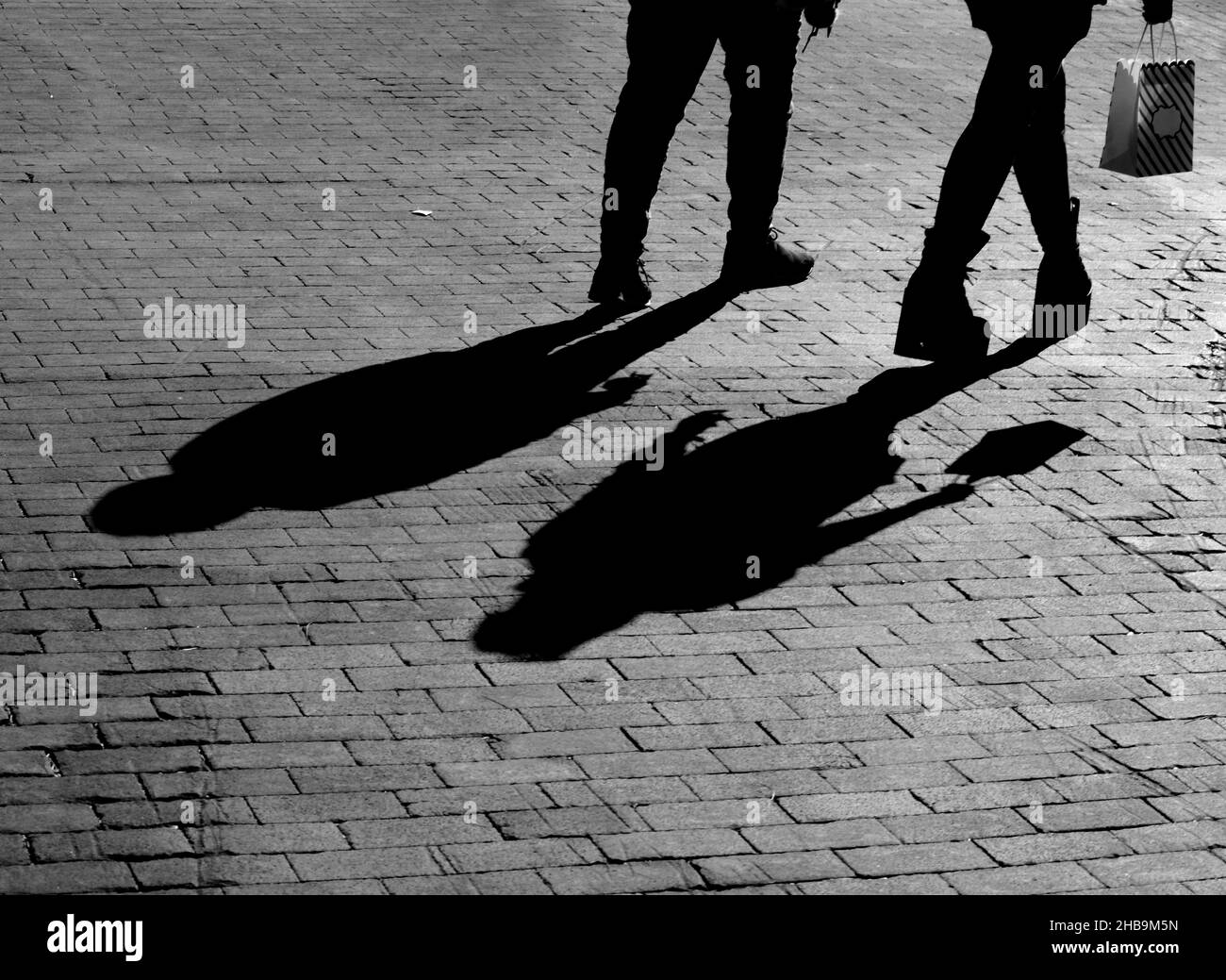Tourists cast long afternoon shadows as they walk along a brick road in downtown Santa Fe, New Mexico. Stock Photo