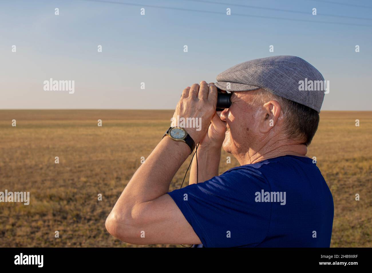 Senior man looking through binoculars in the steppe Stock Photo
