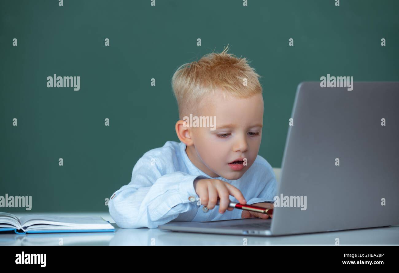 School child using digital pc laptop in class. Portrait of funny pupil of primary school study programming. Funny blonde pupil on blackboard. Stock Photo