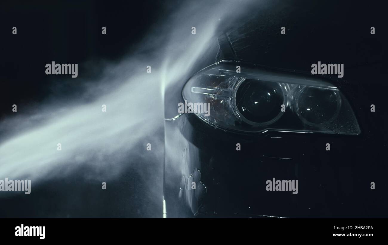 Car headlight wash. Washing modern vehicle body by high pressure jet