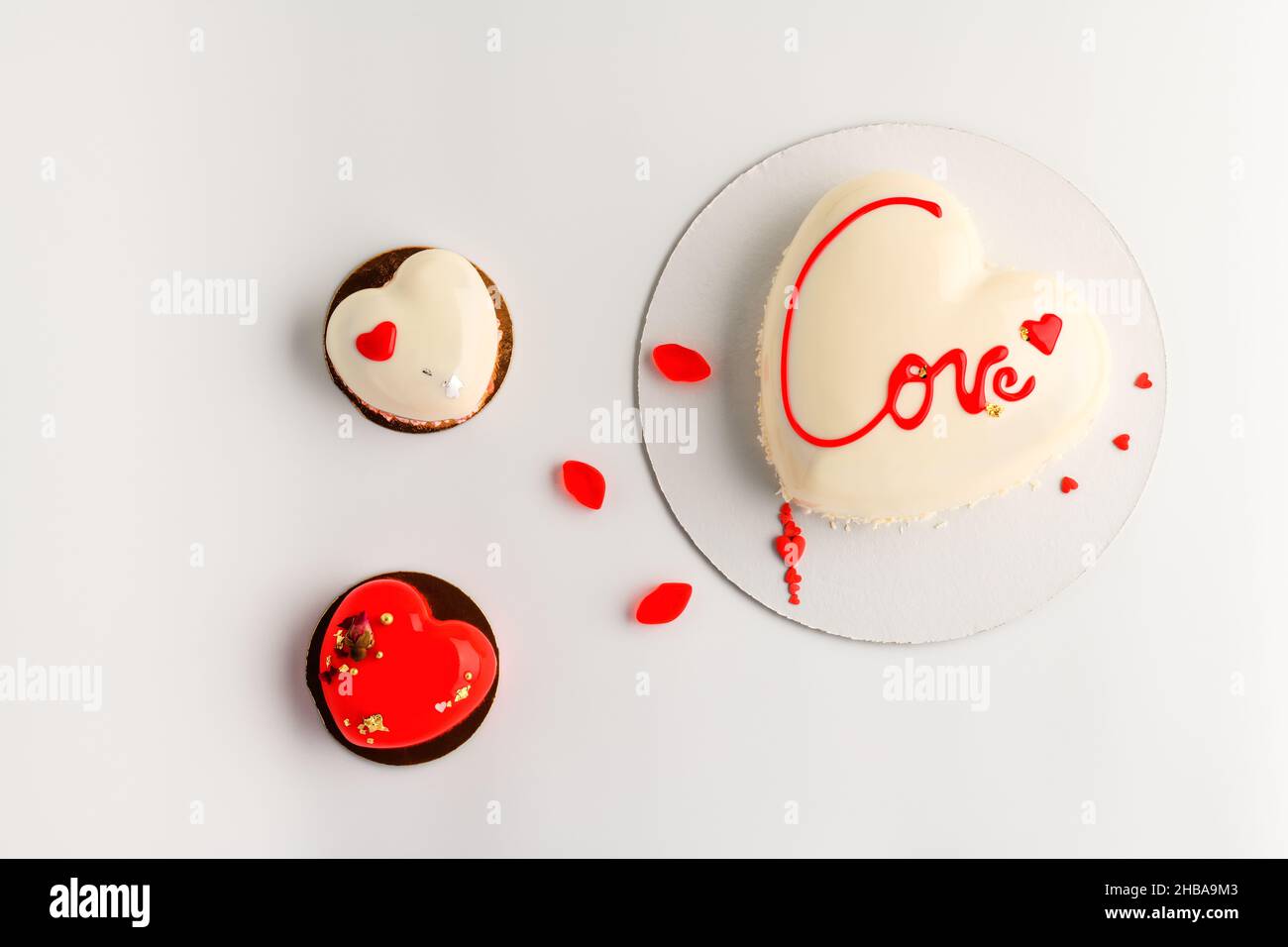 St. Valentine's Day background for bakery, confectionery.  White  mousse cake  and two little cakes in the shape of a heart  on a white background. Stock Photo