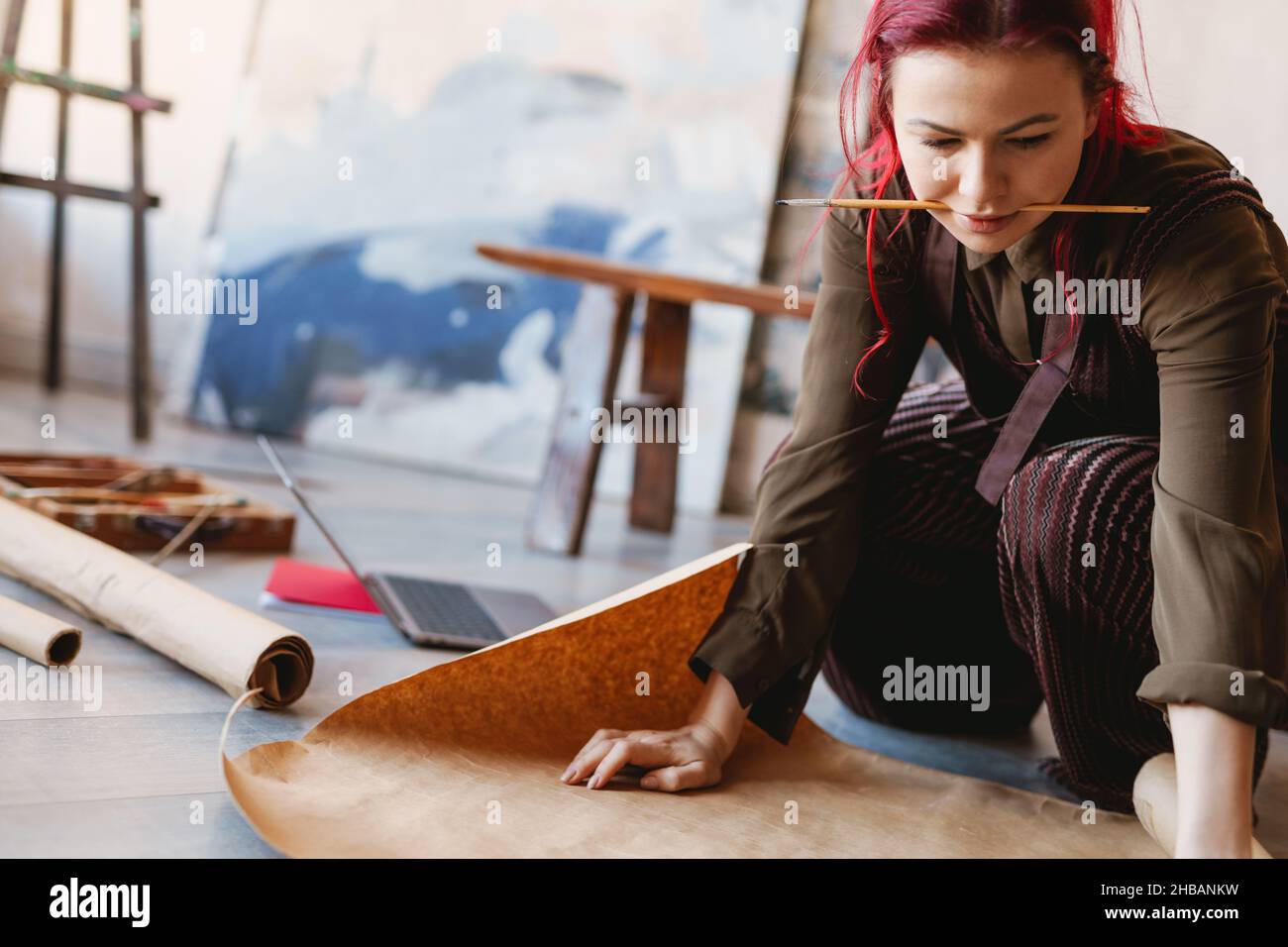 Young woman artist sitting on a floor of an art studio unrolling ...