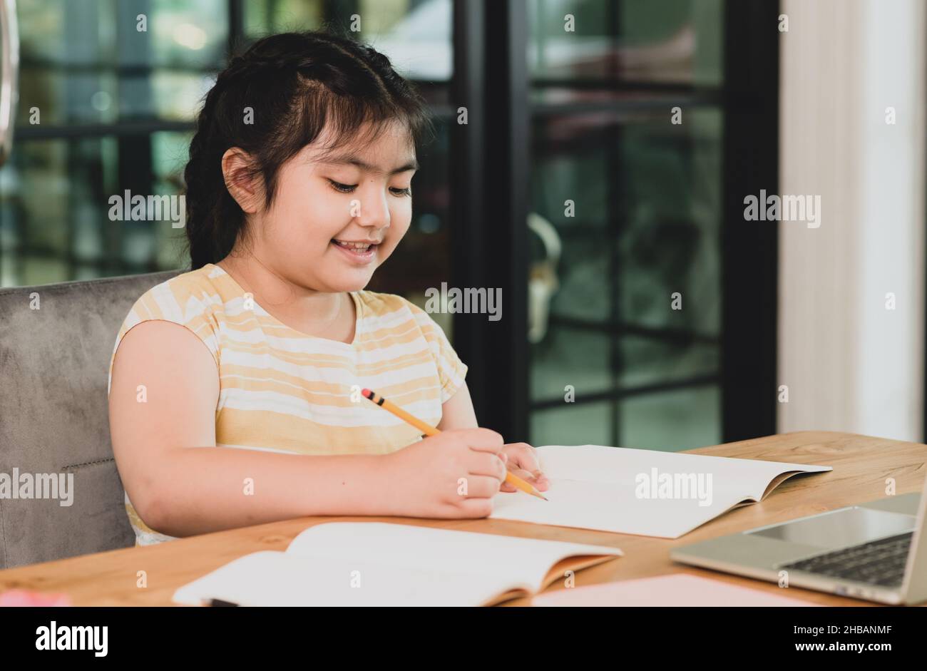 Asian child girl in a good mood studying at home,girl studying online from home,girl doing homework with cheerful expression,online learning. Stock Photo