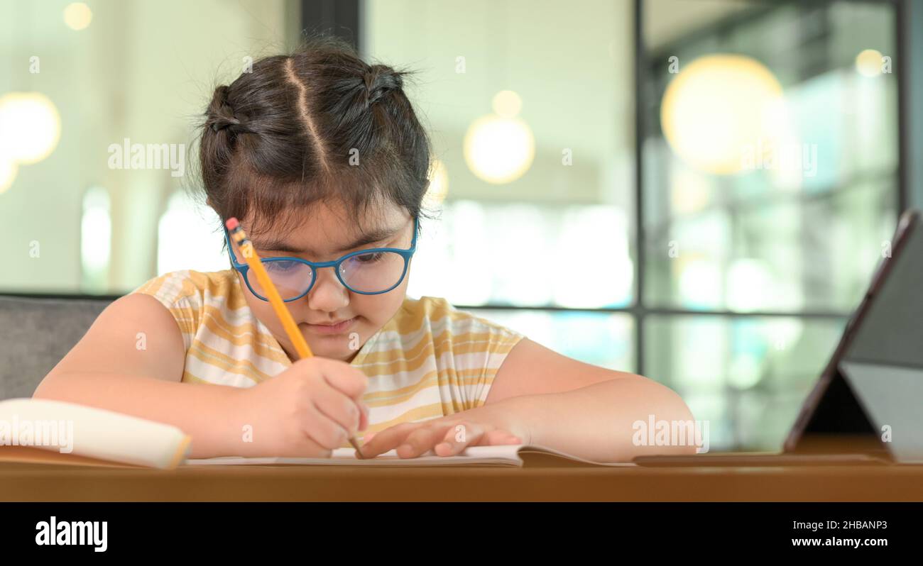 Cropped shot of Asian child girl with glasses is studying at home with serious expression. Online study, Online learning. Stock Photo