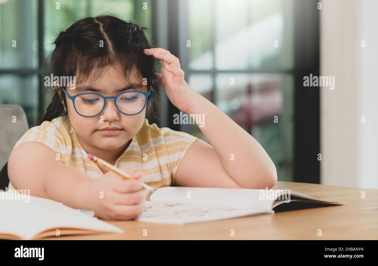Child girl wearing glasses with pencil in hand studying at home bored expression. Online learning. Stock Photo