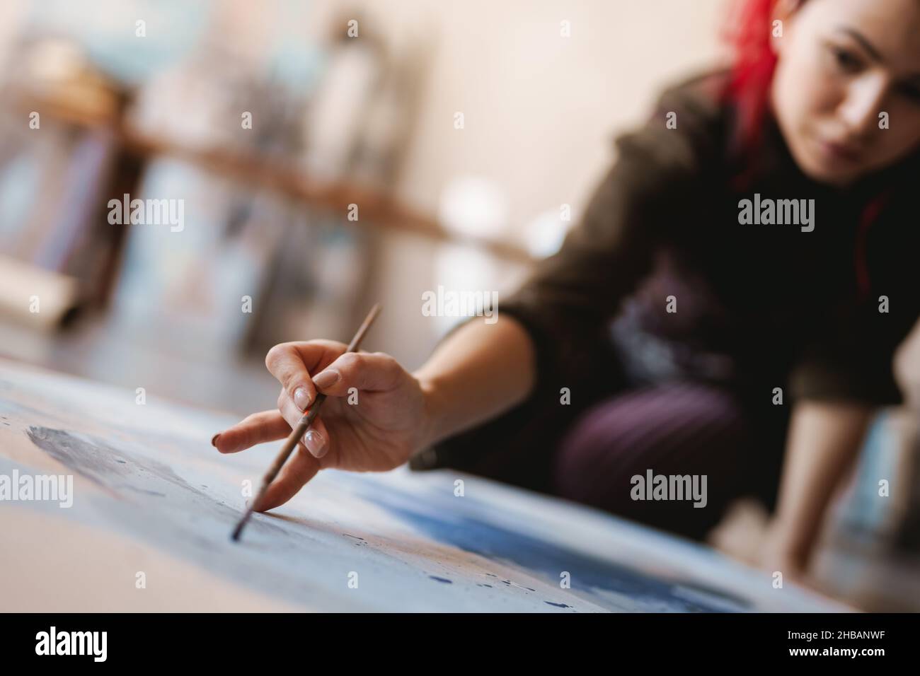 Young woman artist painting while sitting on a floor at an art studio ...