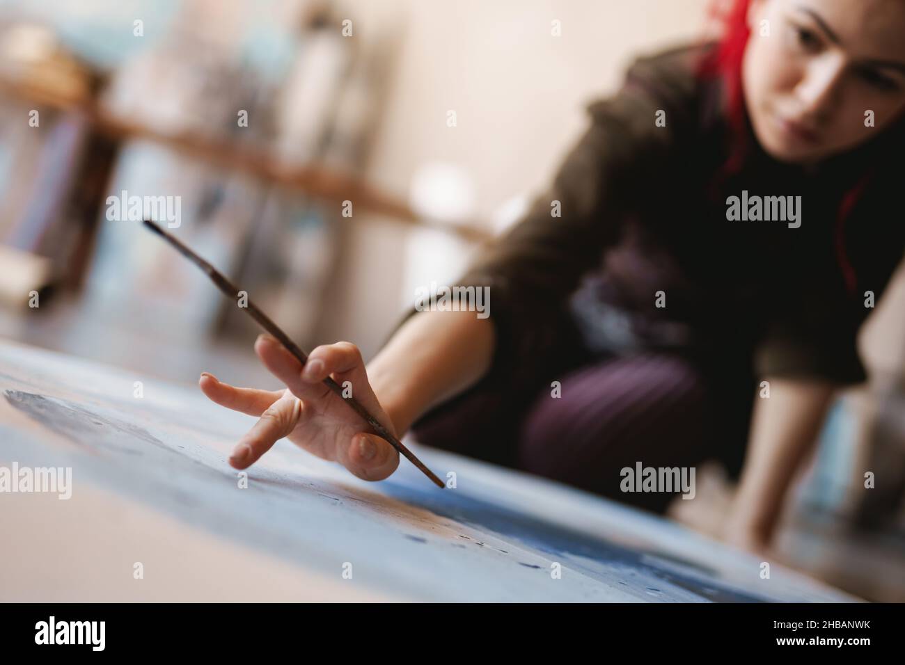 Young woman artist painting while sitting on a floor at an art studio ...