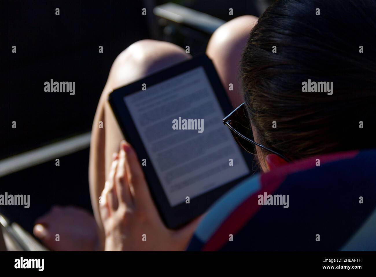 Brecht, Belgium - May 8 2018: A close up portrait of a person reading an e-book on an e-ink e-reader on a sunny day outside in the garden. An easy way Stock Photo