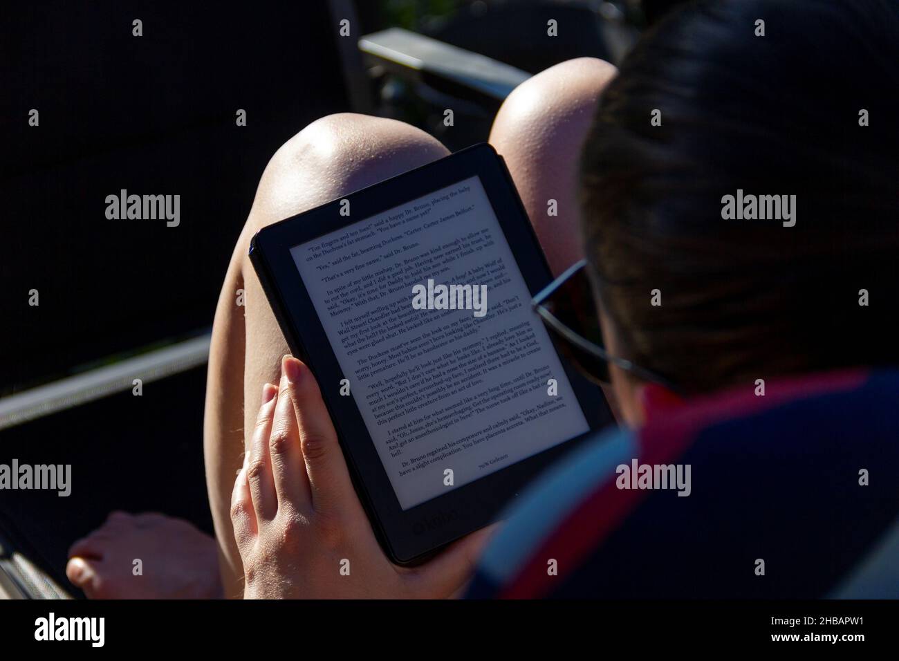 Brecht, Belgium - May 8 2018: A close up portrait of someone reading an e-book on an e-ink e-reader on a sunny day outside in the garden. An easy way Stock Photo