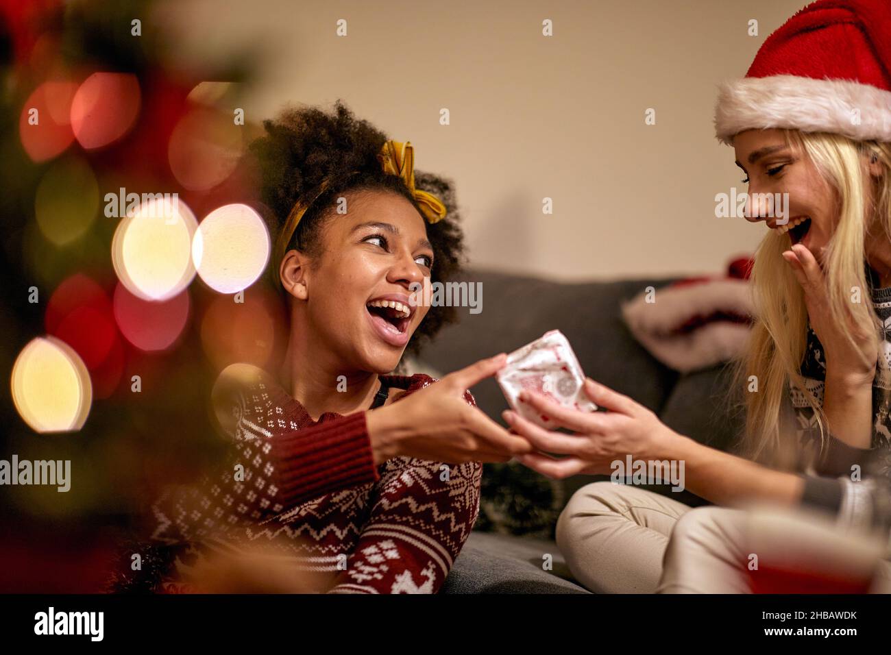 A girl is giving a present to her female friend at New Year party in a festive atmospehre at home. Christmas, New Year, holiday, party Stock Photo