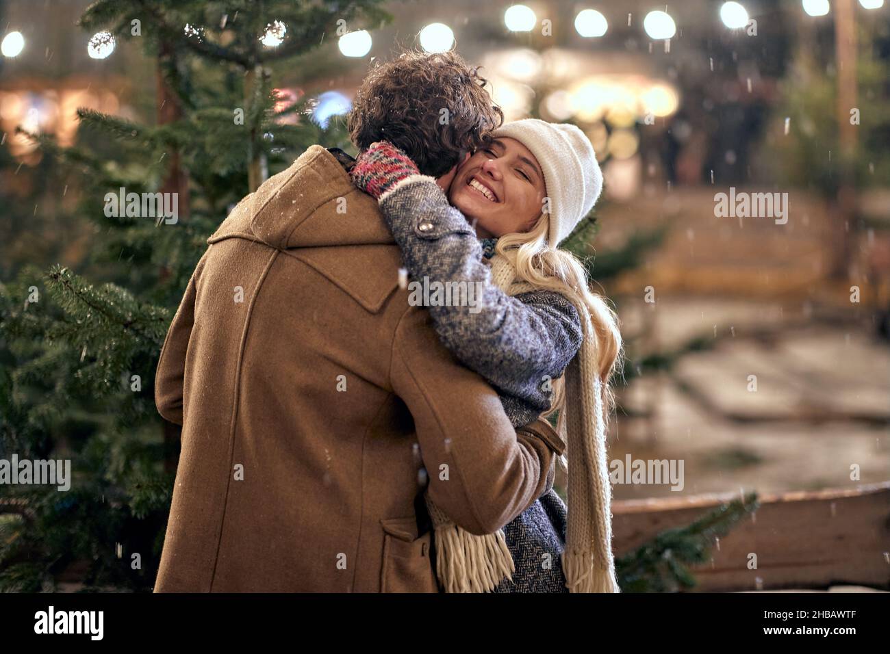 A young couple in love is in hug while enjoying christmas holidays and walking the city on a beautiful snowy night. Christmas, New Year, holiday, love Stock Photo