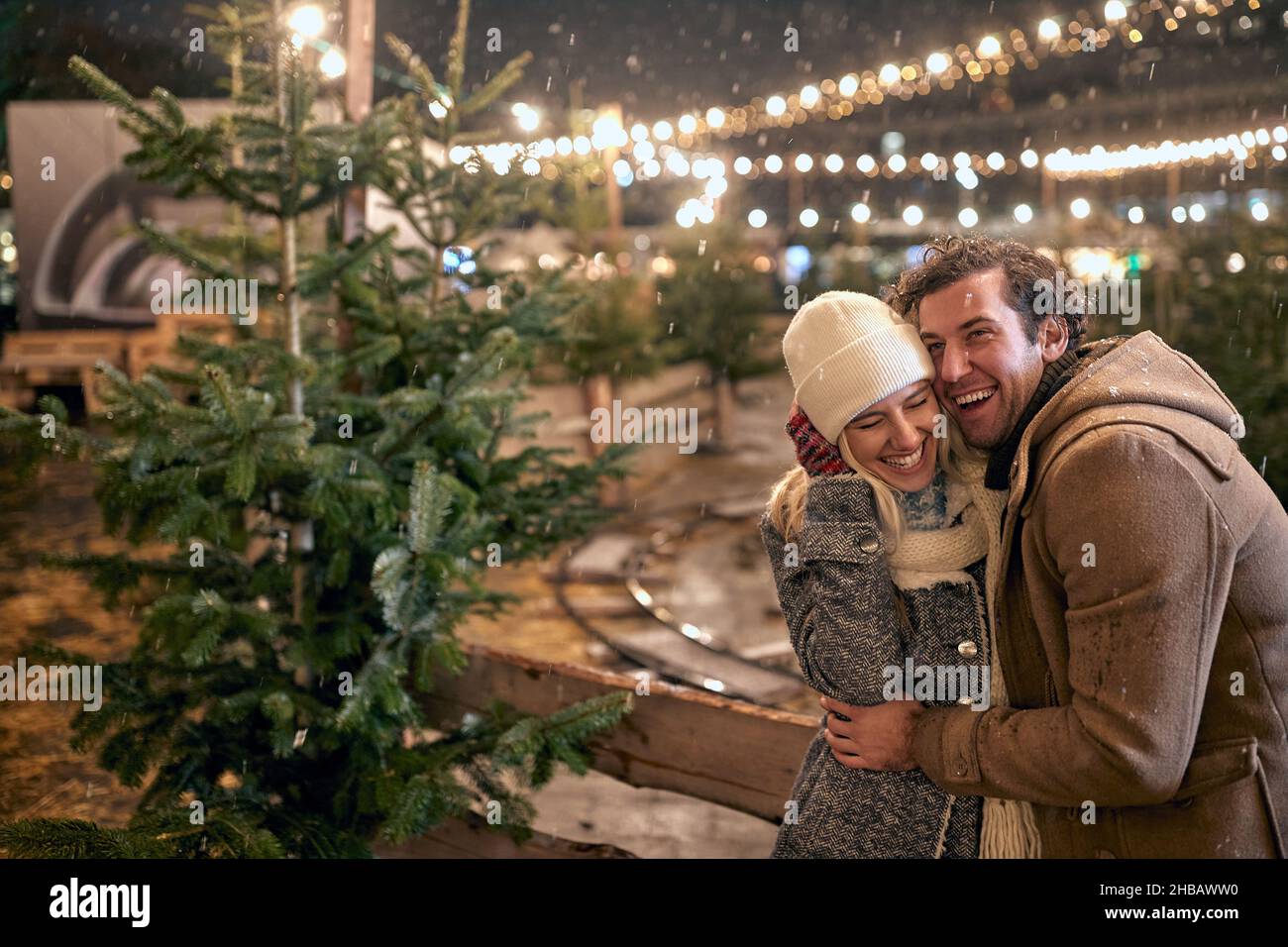 A young cheerful couple in love is having a good time while enjoying christmas holidays and walking the city on a beautiful snowy night. Christmas, Ne Stock Photo