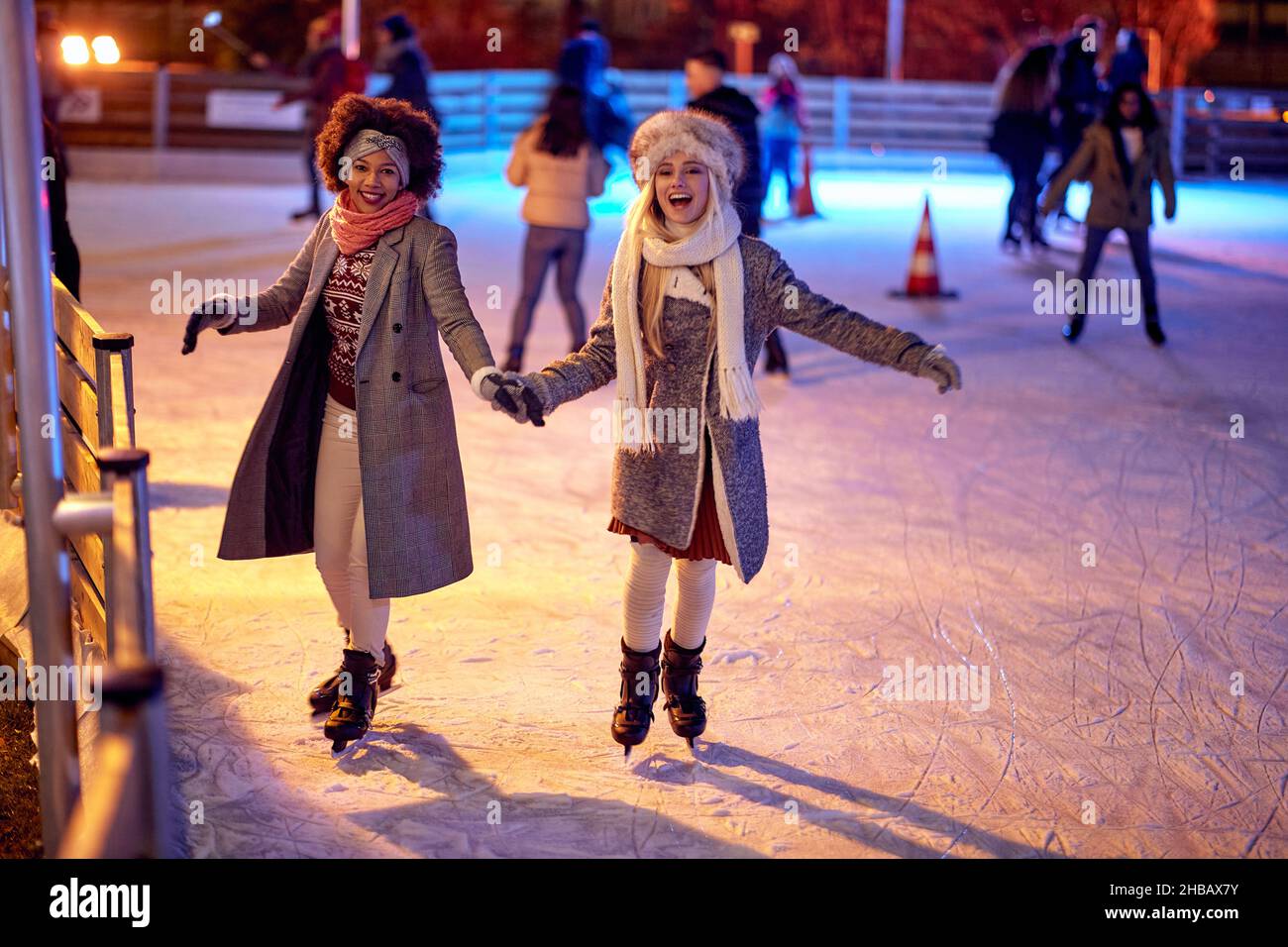 Beautiful gilfriends ice skating together at night; Winter joy concept Stock Photo