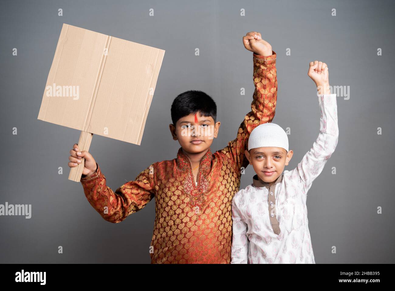 Multiethnic kids protesting by holding empty sign board on gray background - concept of protest against communal violence and religious inequality Stock Photo