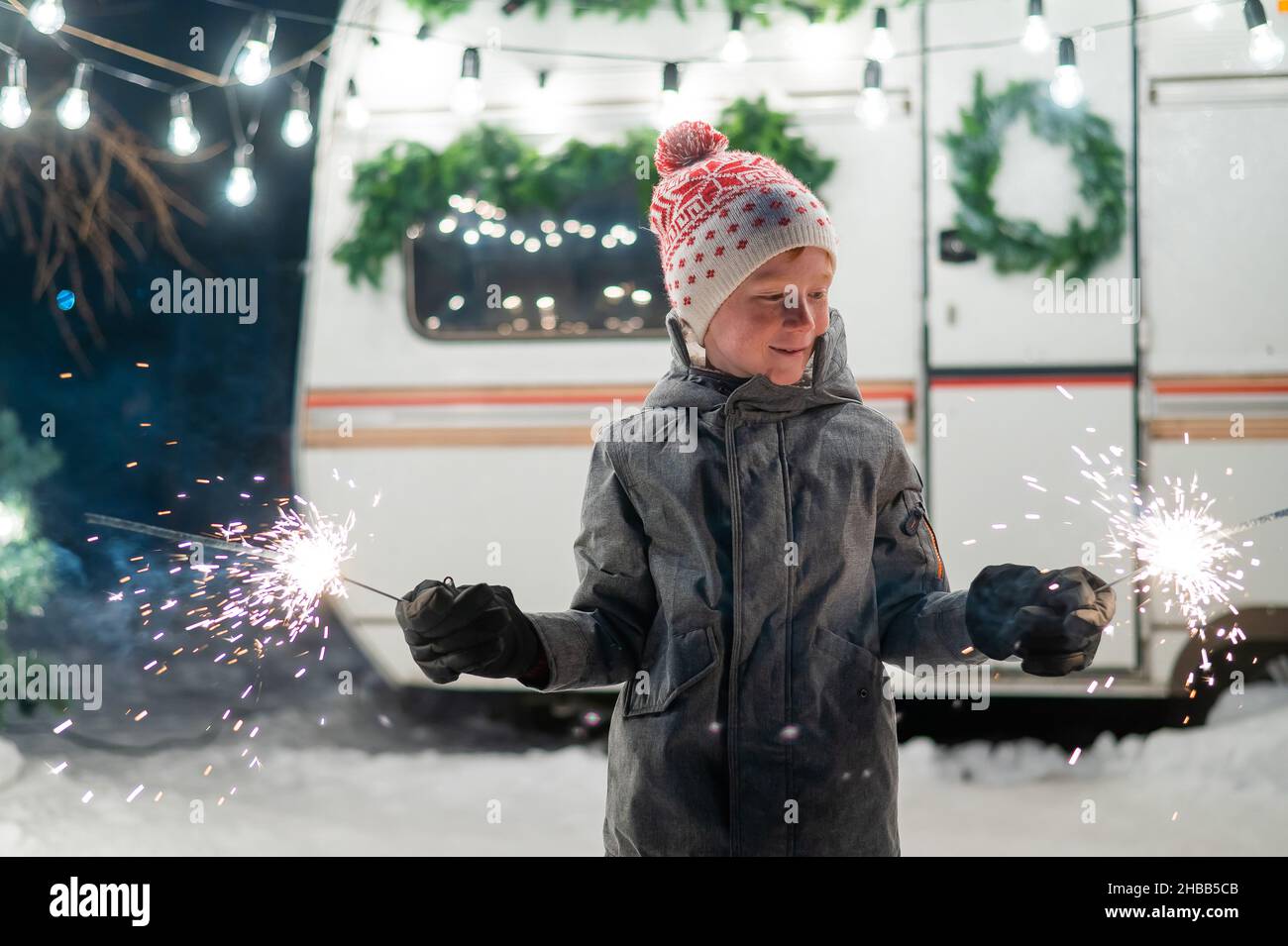 Caucasian red-haired boy holding sparklers by the trailer. Schoolboy celebrates Christmas on a trip. Stock Photo