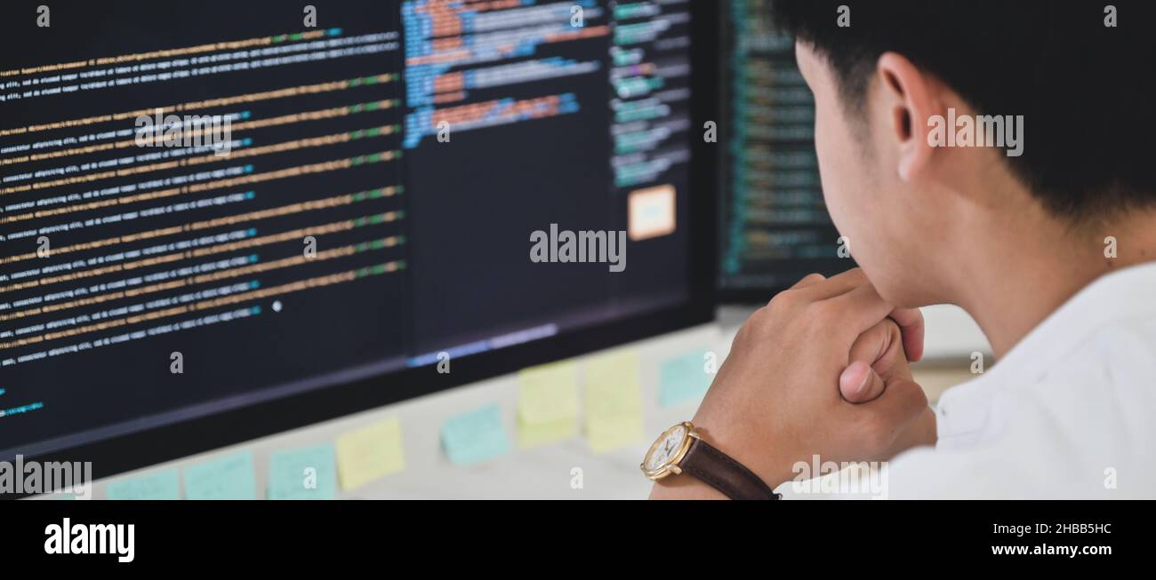 A male programmer sits and watches the code on a computer monitor to ...