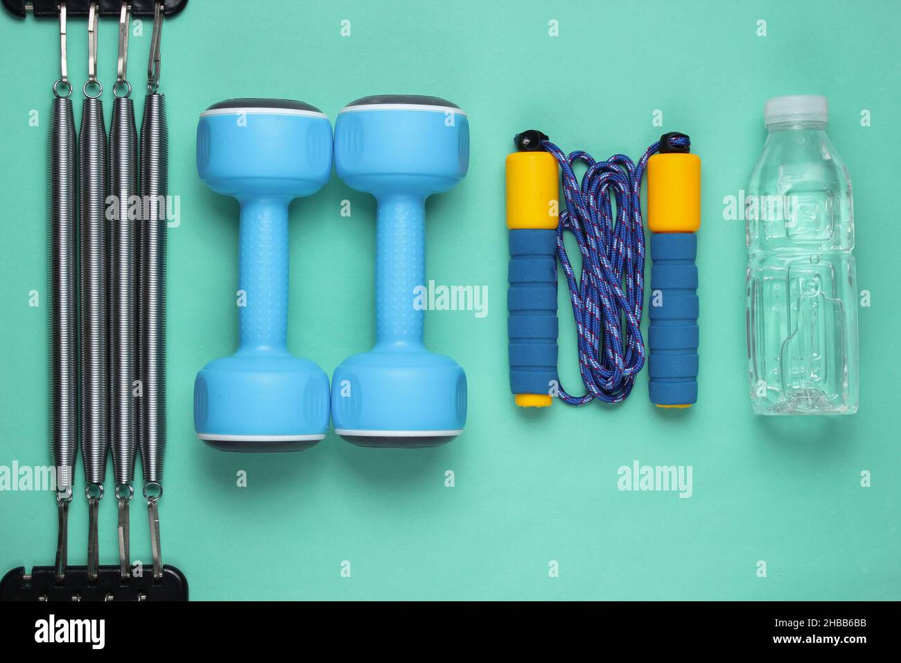 Fitness background. Equipment for gym and home. Jump rope, dumbbells,  expander, water on pastel pink background top view copy space Stock Photo