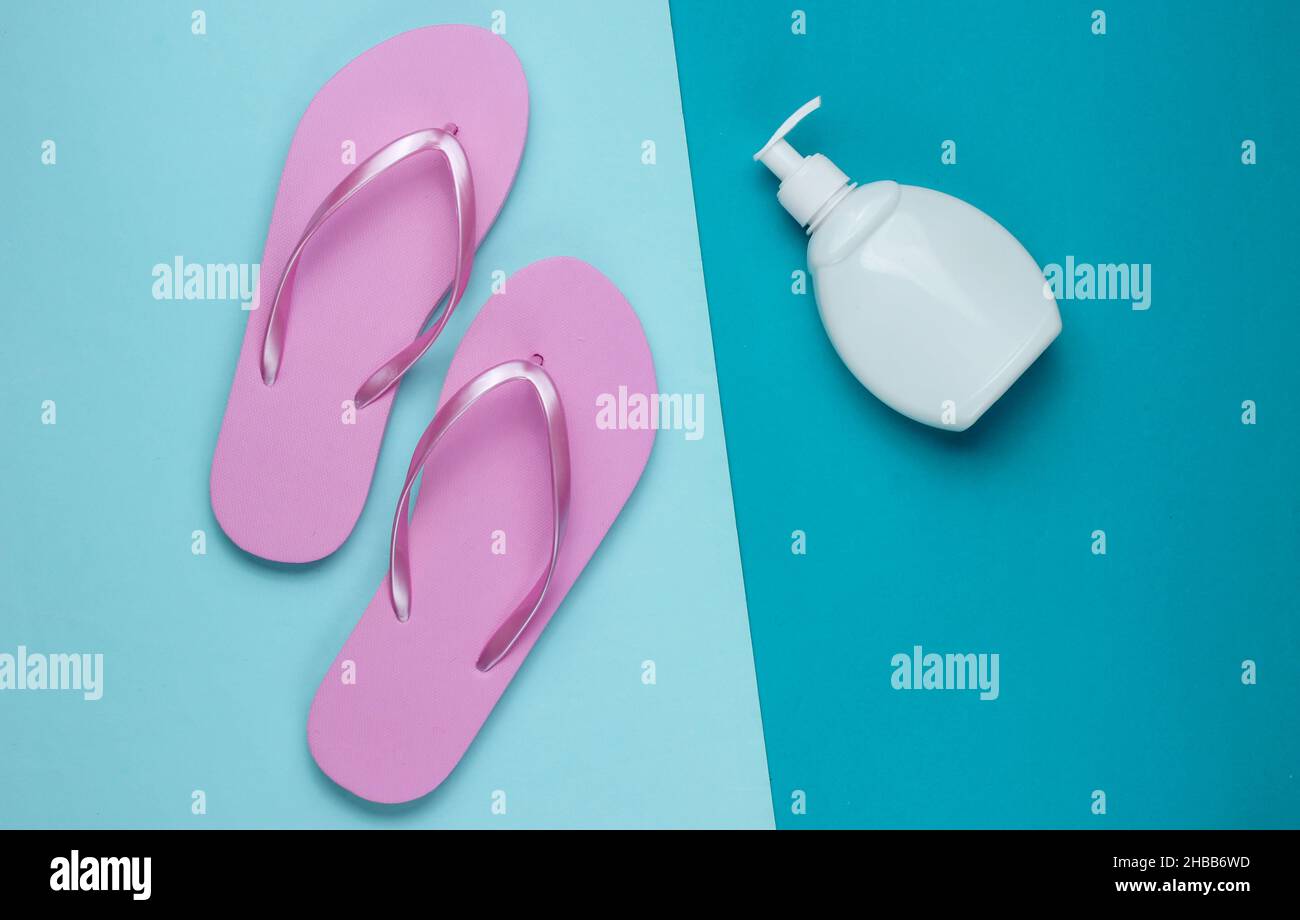Beach accessories. Fashionable beach pink flip flops, sunblock bottle on blue paper background. Flat lay. Top view Stock Photo