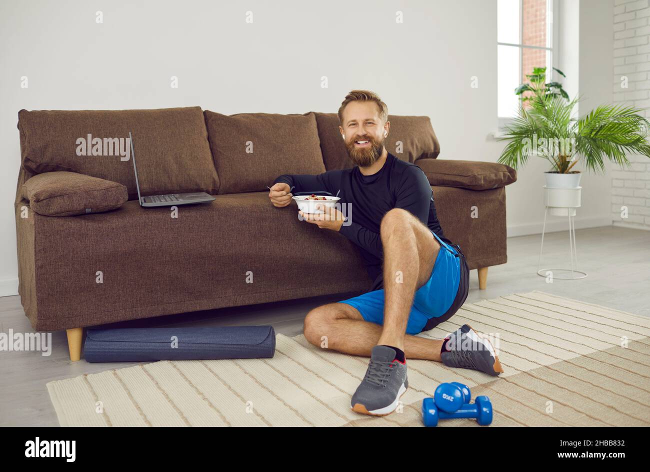 Happy man having break during his home workout, eating healthy food and using laptop Stock Photo