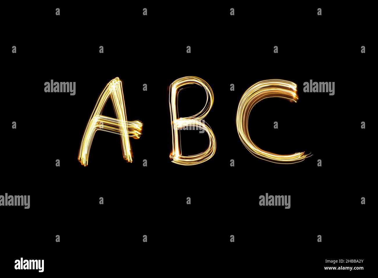 Neon ABC letters, light painting yellow alphabet against black background. Long exposure photography. Stock Photo
