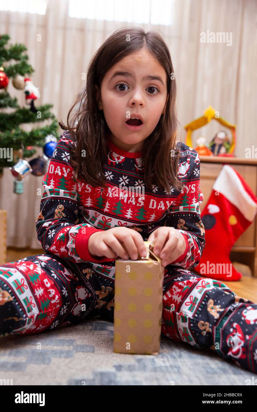 Caucasian little girl with amazed face opening Christmas day gift. Stock Photo