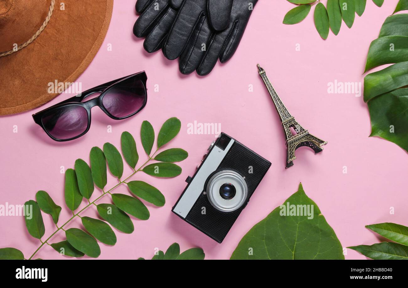 Jorney to Paris. Women's accessories, retro camera, figurine of the Eiffel tower on pink pastel background with green leaves. Top view Stock Photo