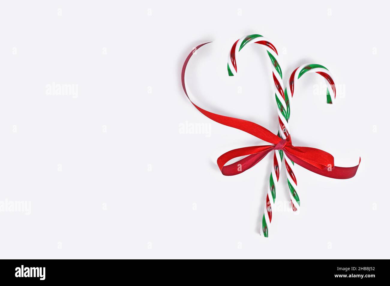Striped candy canes tied together with red ribbon on side of white background with copy space Stock Photo