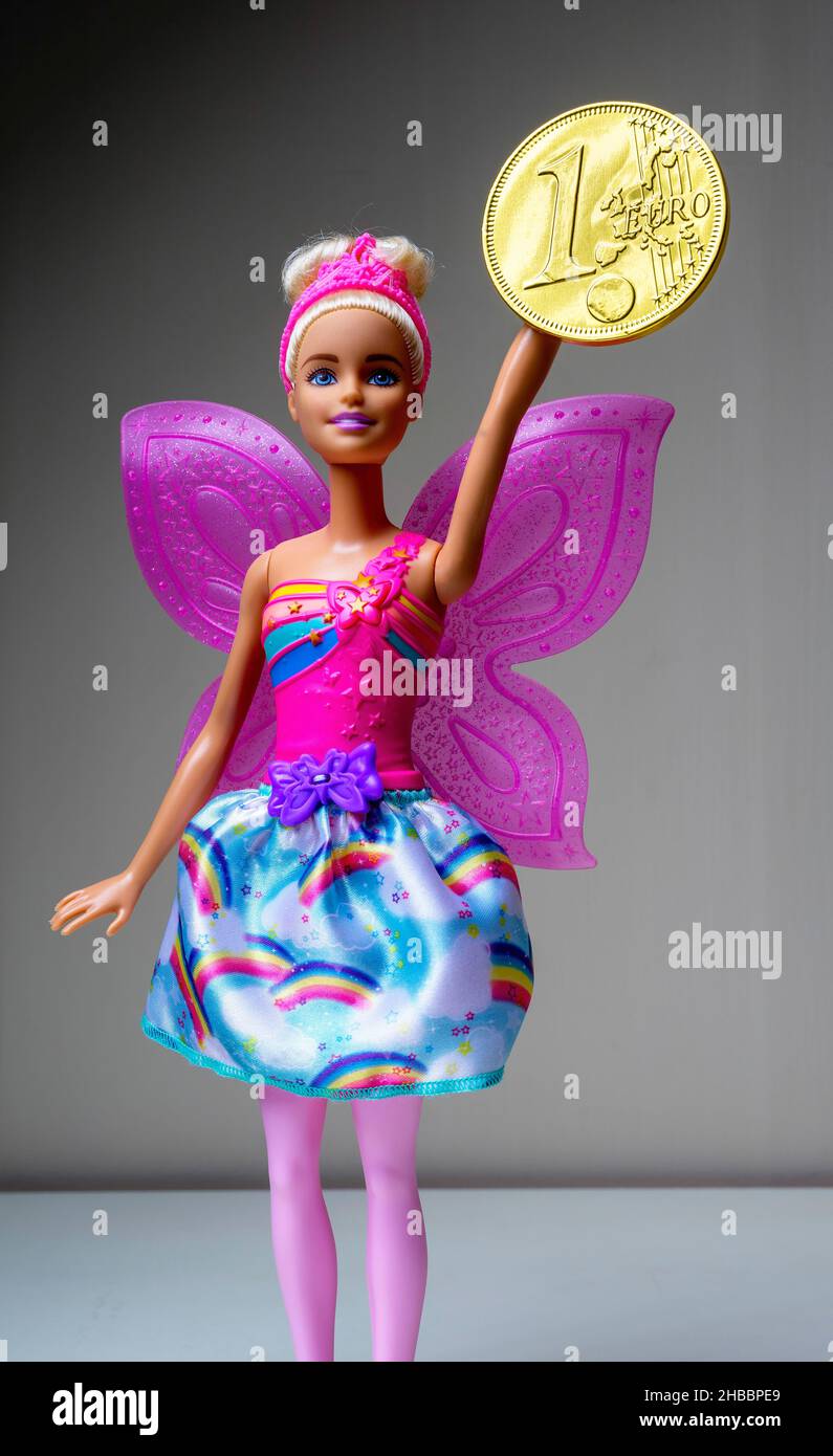 Barbie doll with pink wings holding a chocolate wrapped with embossed 1 Euro coin golden foil, Stock Photo