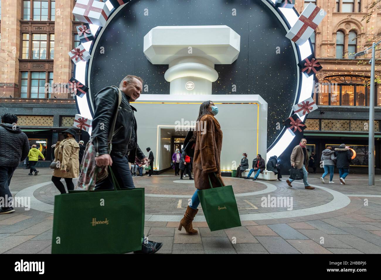 London, UK. 18 December 2021. Shoppers with green Harrods bags outside the  Chanel Christmas decorations at Harrods flagship store in Knightsbridge. In  an unusual move, instead of on Boxing Day, the company