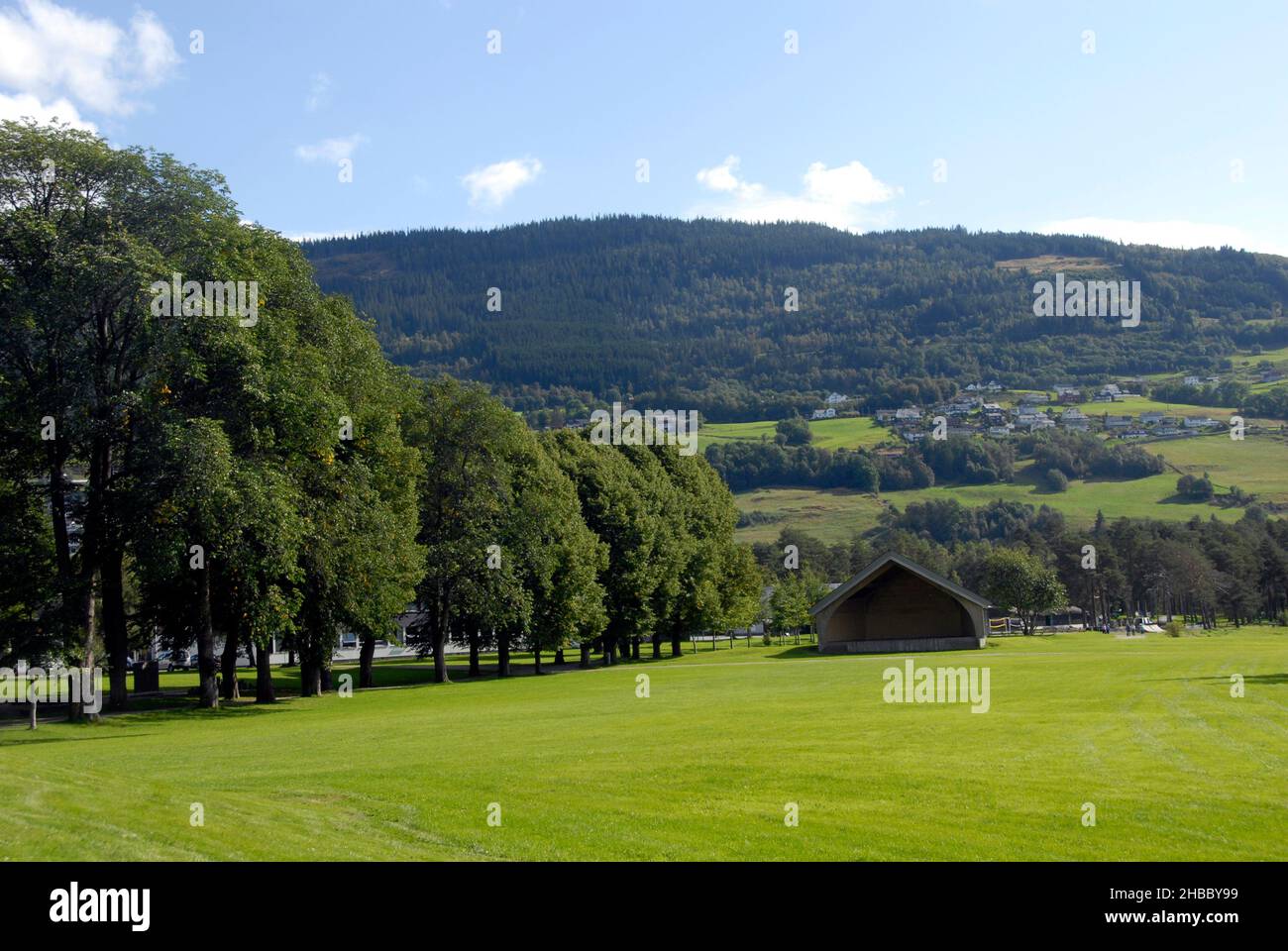 Attractive grassy open area with small building and line of trees to one side and mountains beyond, Norway Stock Photo