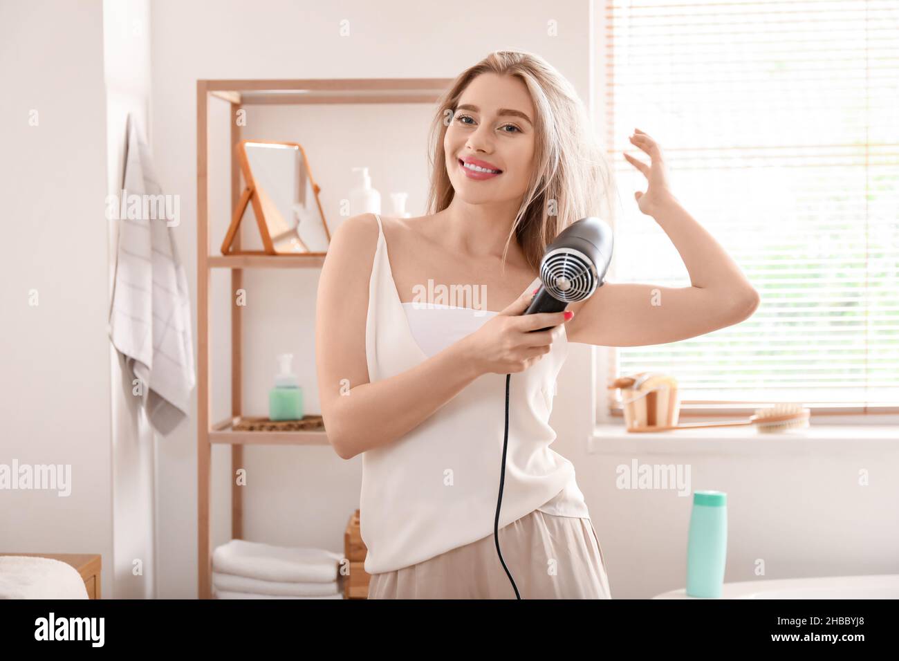 Pretty young woman blow drying her hair in bathroom Stock Photo - Alamy
