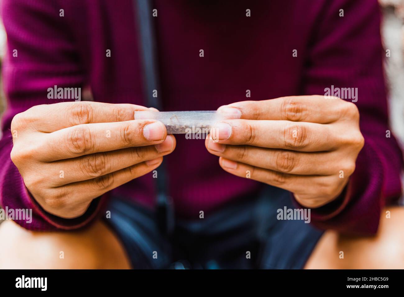 A young man uses cigarette paper to roll a cigarette on a street Stock