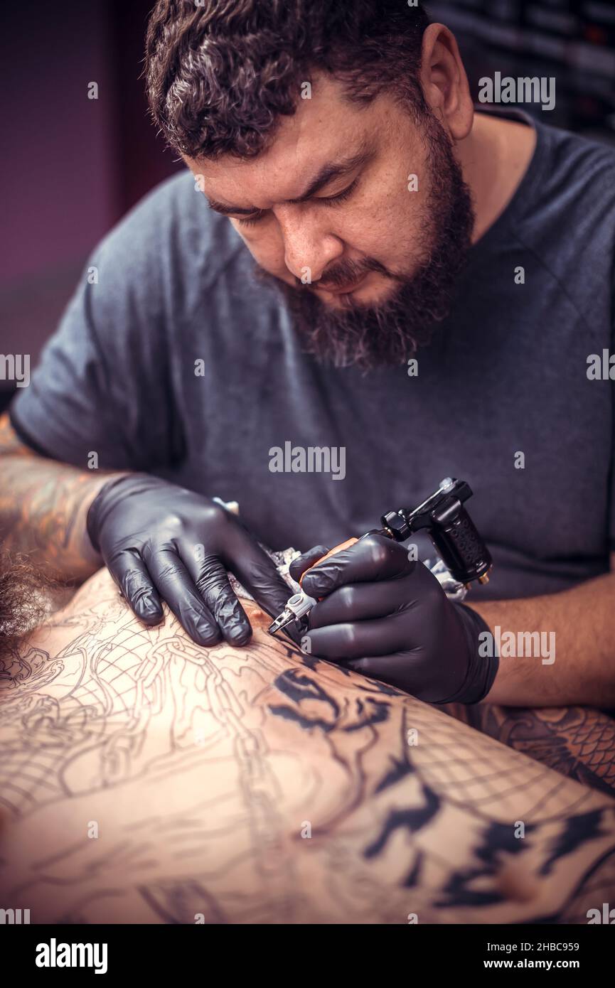 Professional tattooer makes a tattoo on the skin in studio Stock Photo